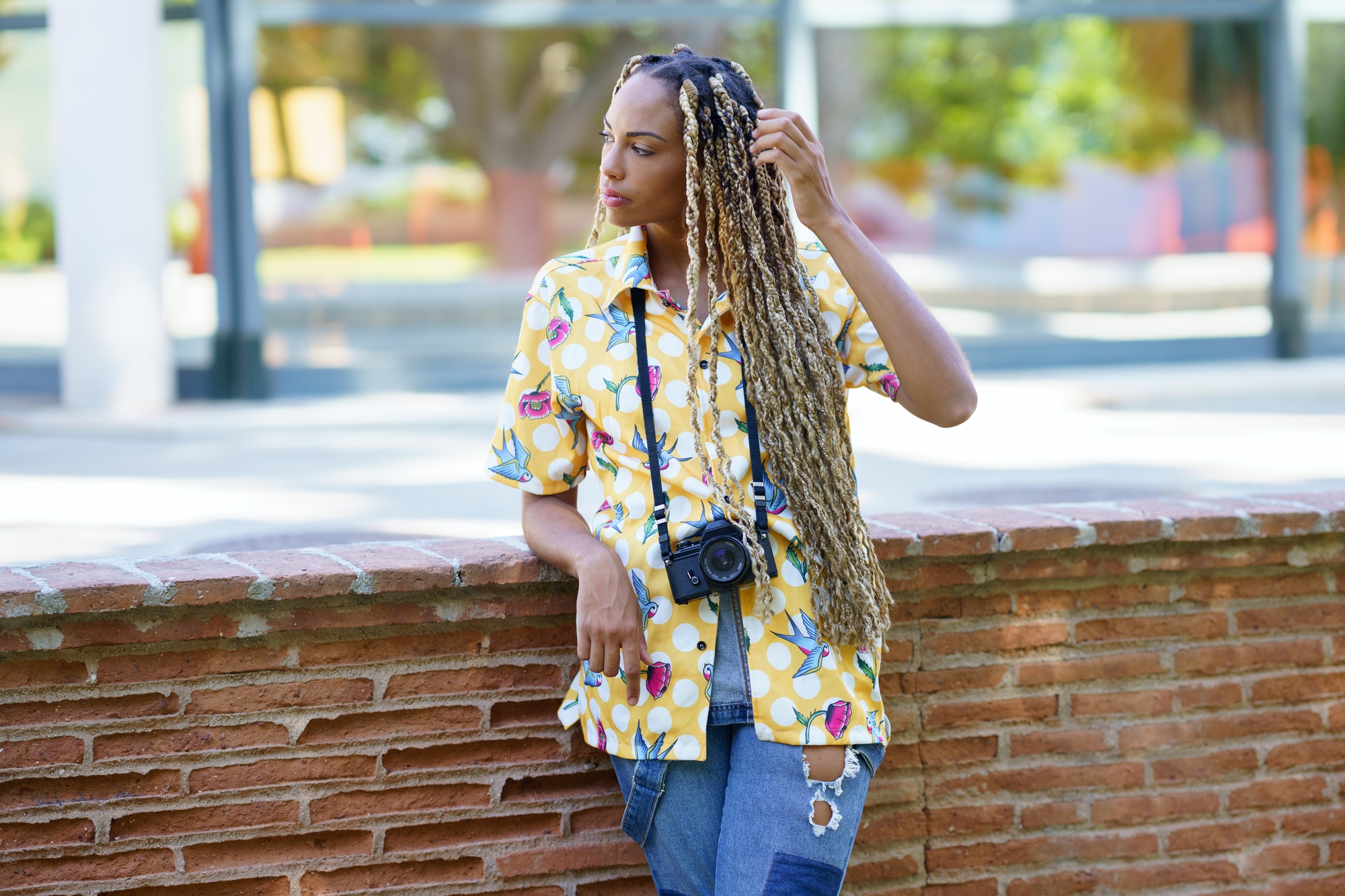 African influencer combed with colorful braids standing with a camera outdoors.