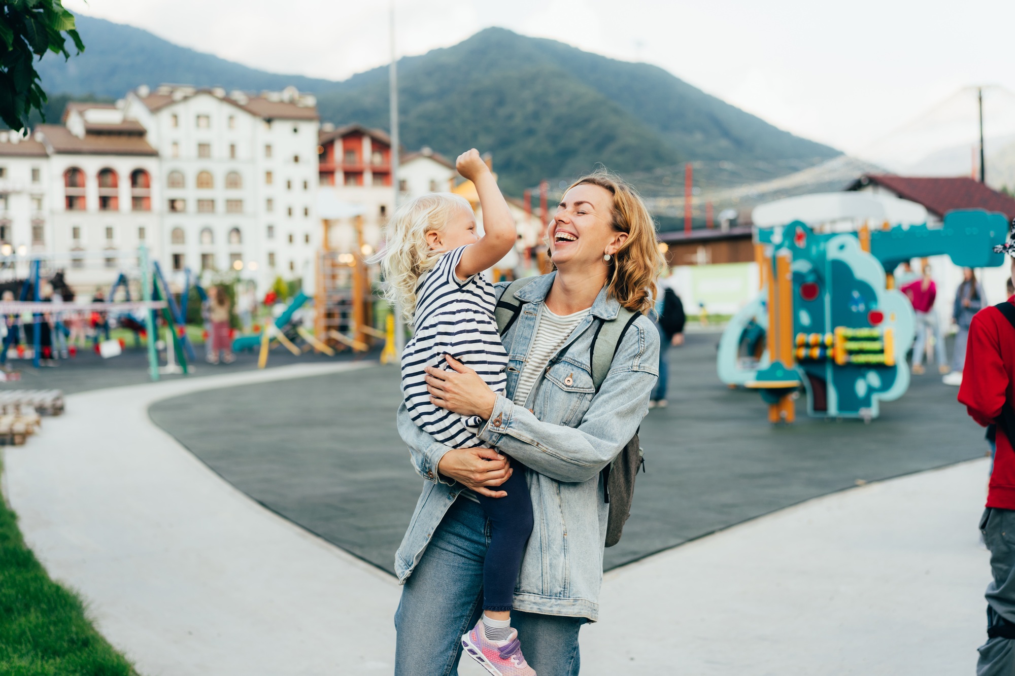 Happy laughing mother holding her little daughter in her arms is walking in the city.